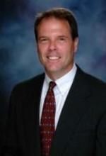 Man in suit and tie smiling against a blurred blue background.