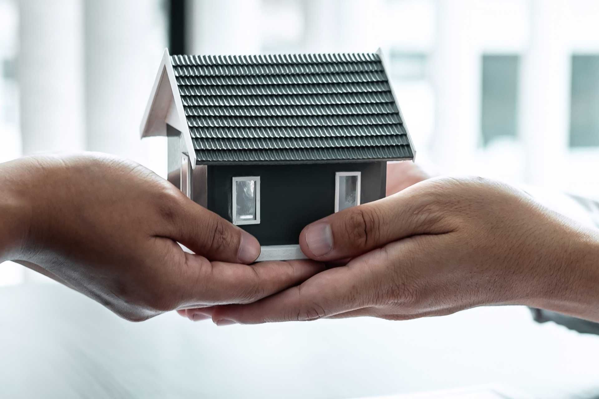Hands holding a miniature house, symbolizing a property transaction.