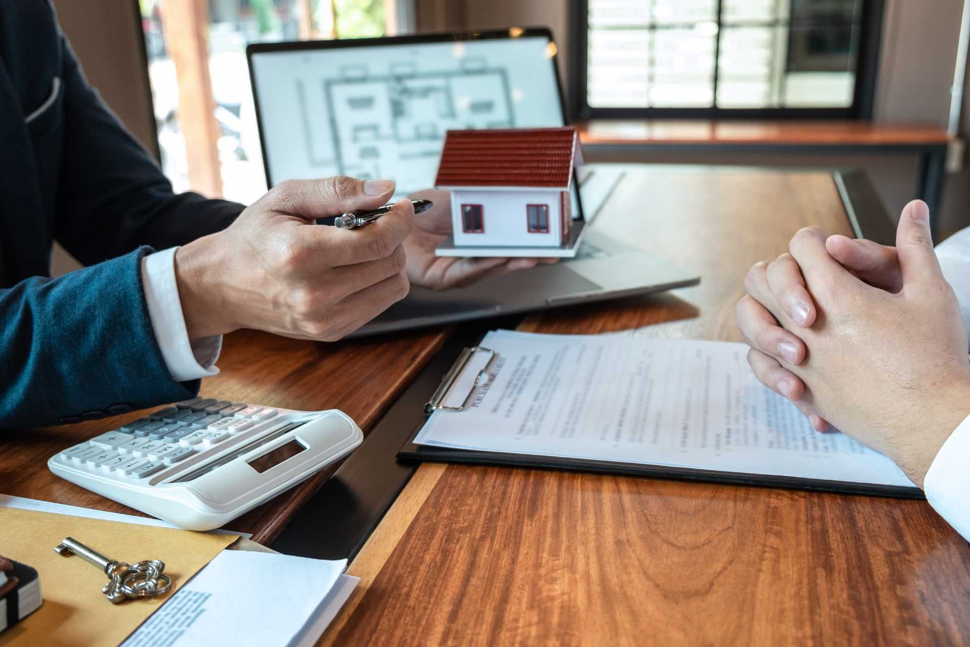 Real estate agent pointing at a model house and paperwork at a desk.