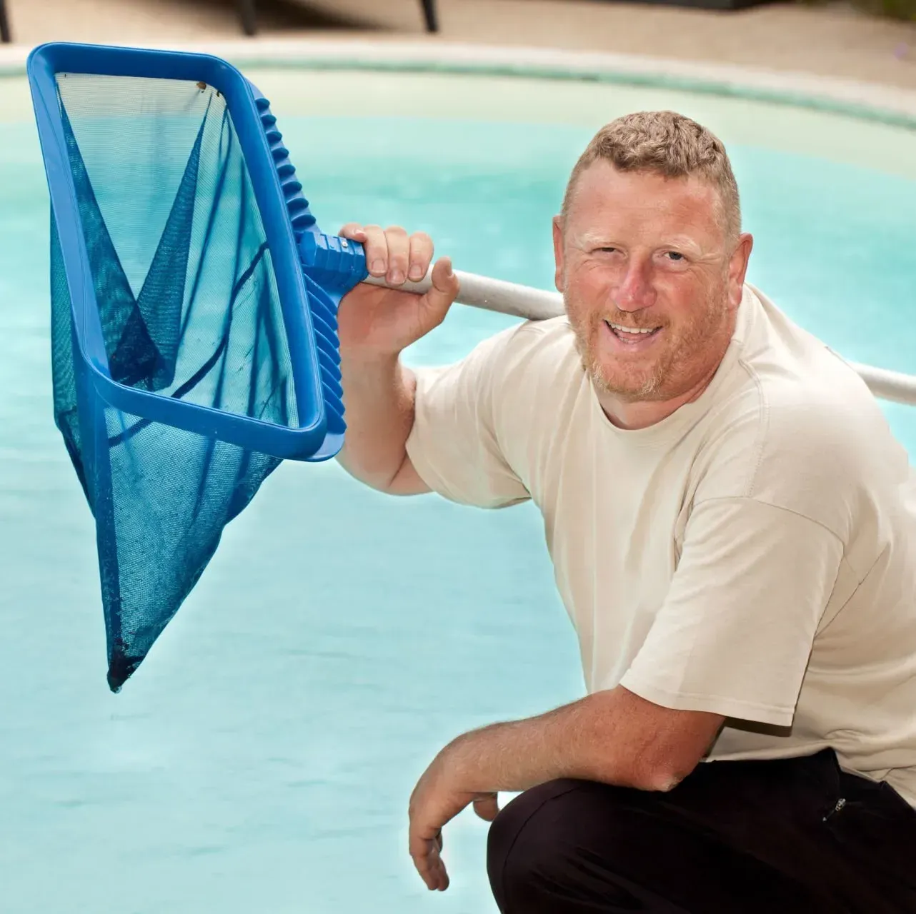 A man holding a blue net in front of a pool
