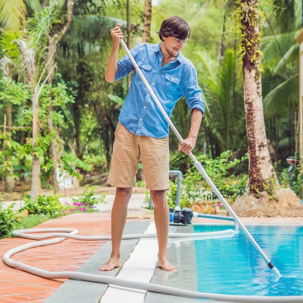 A man is cleaning a swimming pool with a hose.