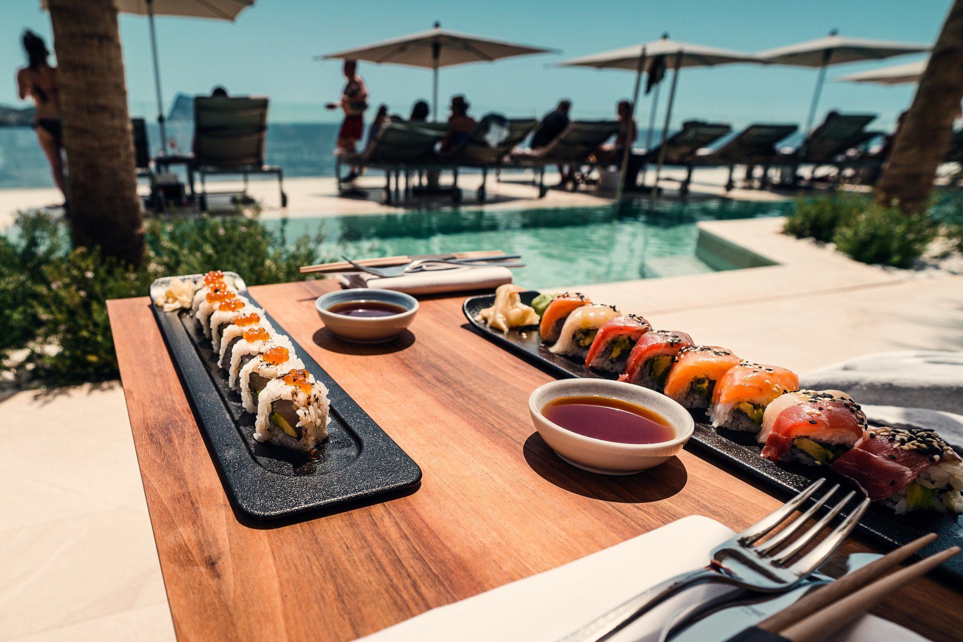 A wooden table topped with plates of sushi and dipping sauce.