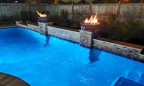 A large swimming pool with a fire pit in the middle of it at night.