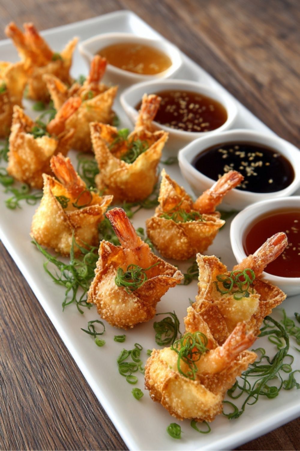 A long white platter holds crispy fried shrimp wontons garnished with green onions, served with four small dipping sauces.