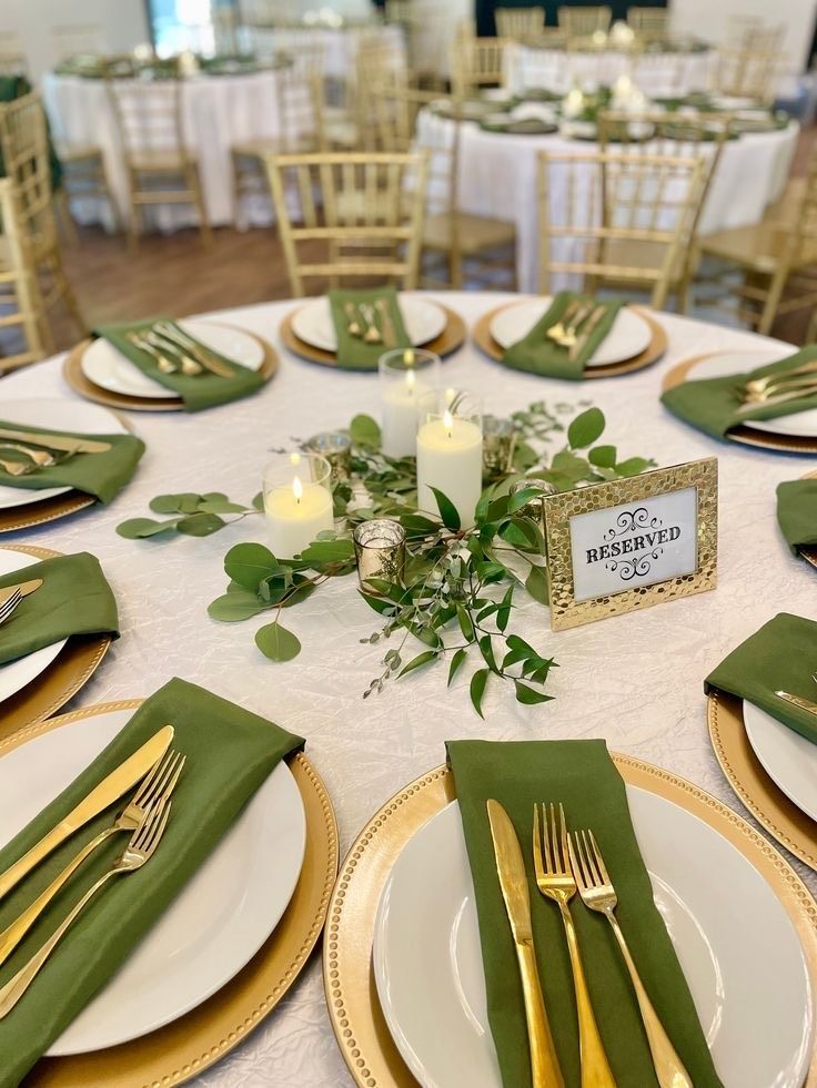A formal table setting at an event with gold chargers, white plates, olive napkins, gold cutlery, and a floral centerpiece.