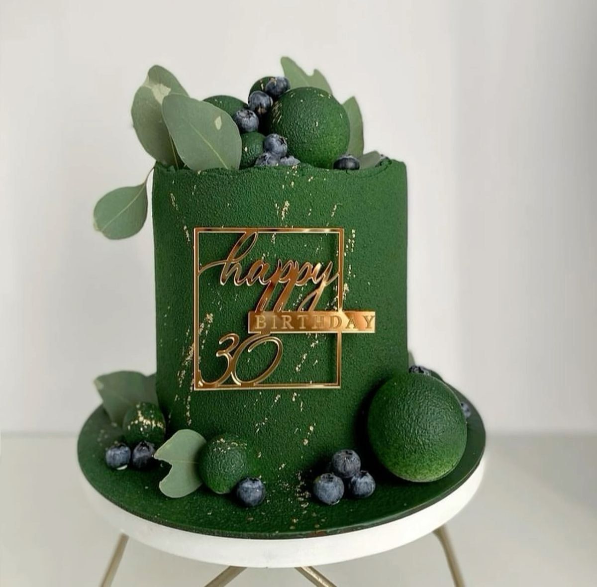A tall, dark green velvet-textured birthday cake adorned with gold 