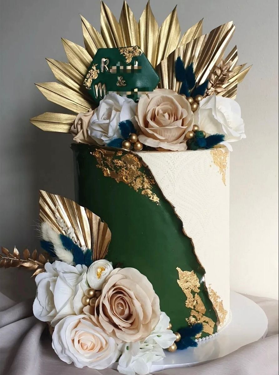 A two-tiered green and white cake decorated with gold leaf, gold palm leaves, and beige and white flowers.