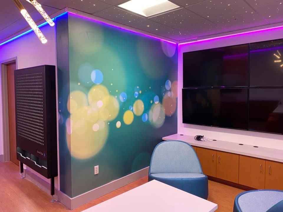 Room with colorful wall mural, LED lights, seating, and a large display screen.