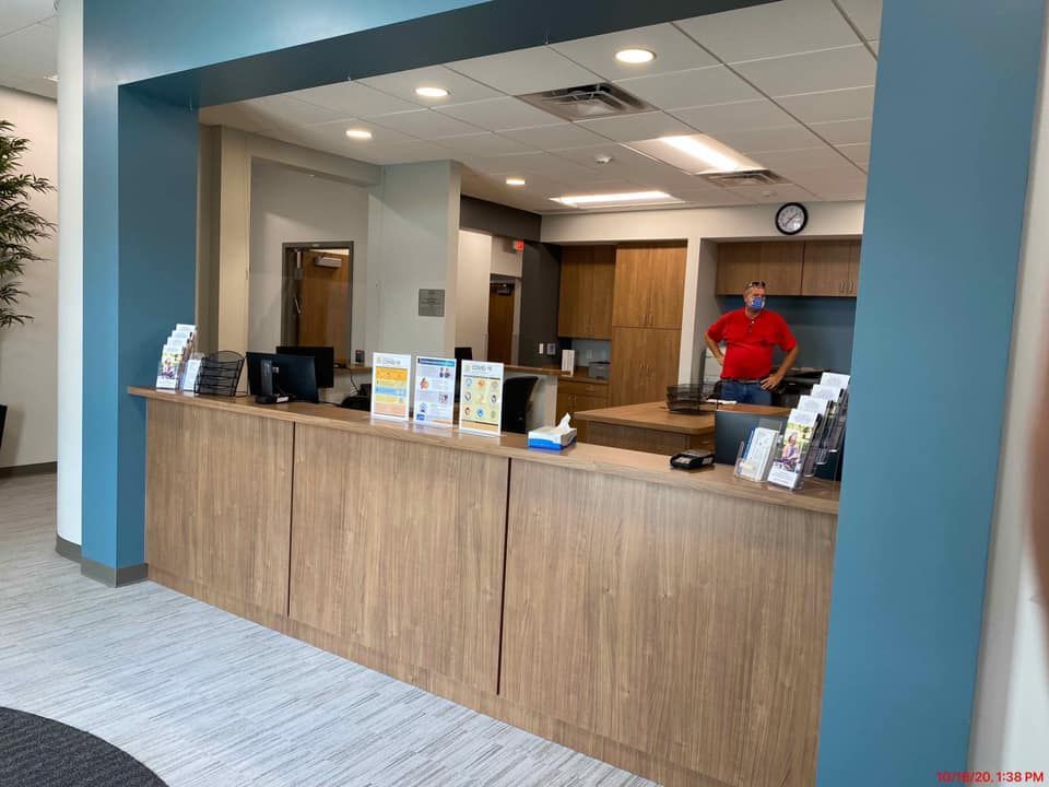 Reception desk with person in red shirt behind it. Wooden cabinets, blue and white walls, indoor.