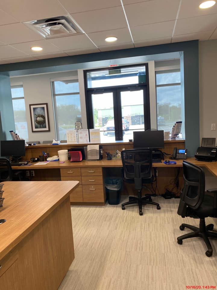 Office reception area with light wood desks, computers, and a door to the outside.