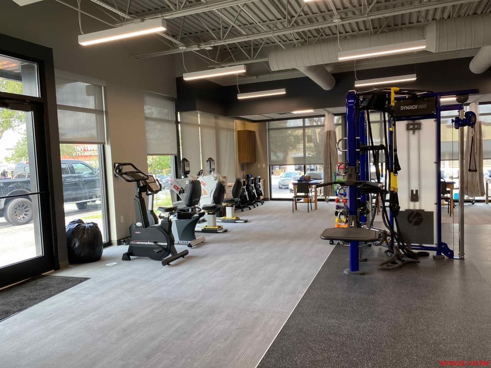 A brightly lit gym with exercise bikes and machines near large windows.