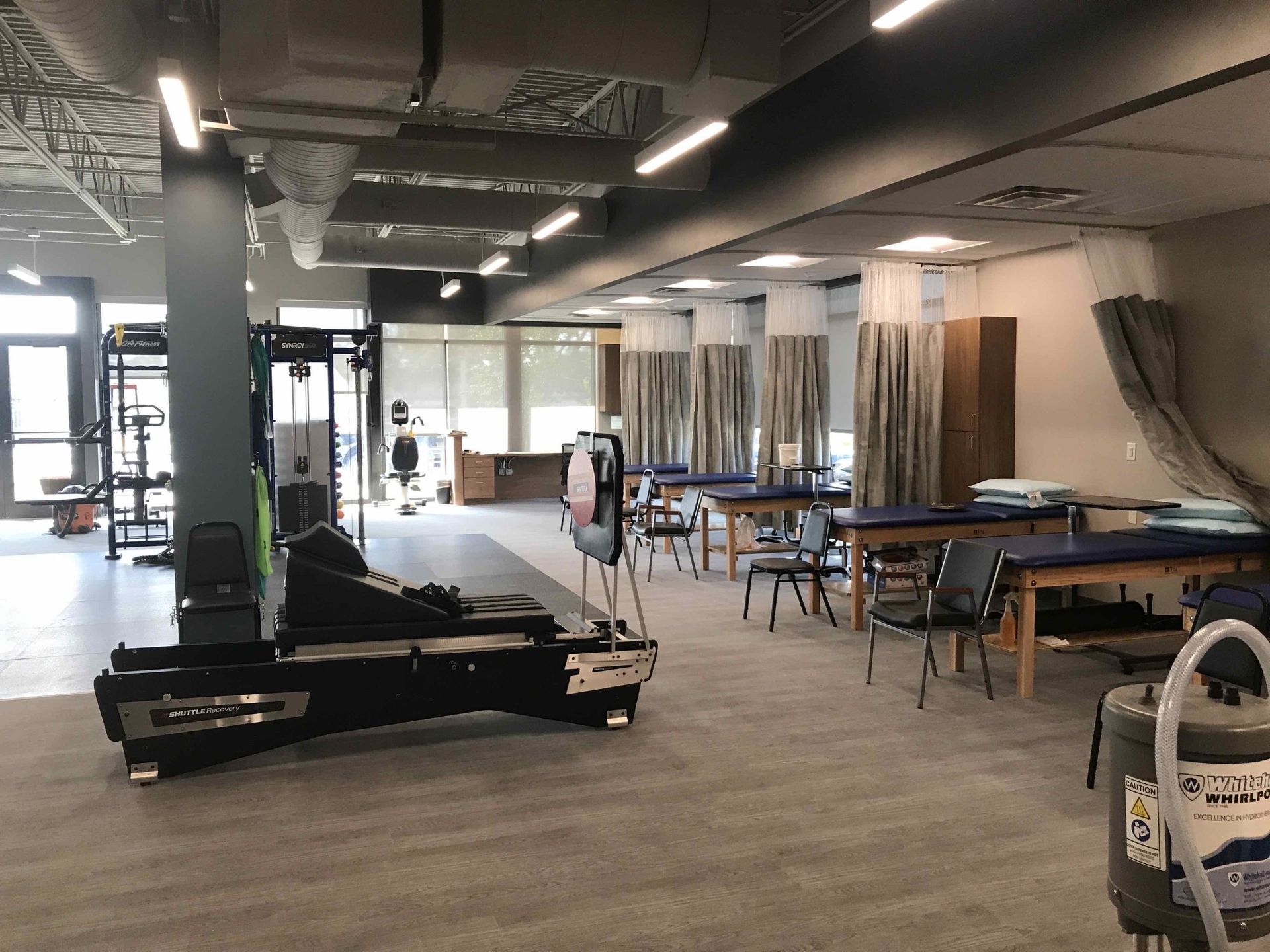 Interior of a physical therapy clinic with exercise equipment, treatment tables, and curtains.
