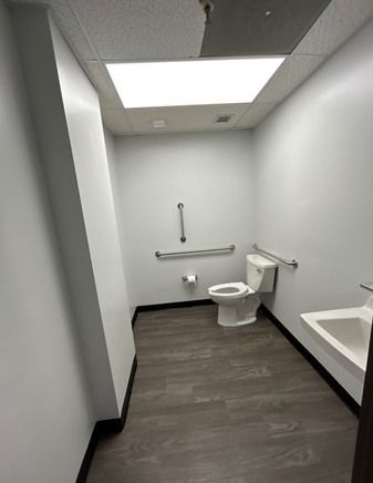 Wheelchair accessible restroom with grab bars, toilet, and sink. Dark gray floor and white walls.