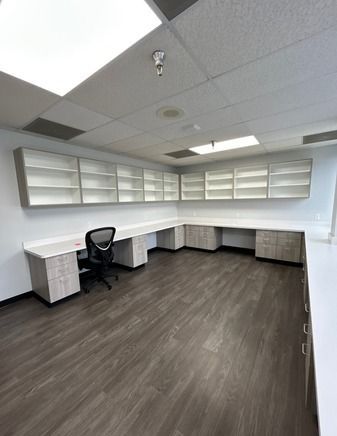 Office space with gray wood-look floor, light desks, cabinets, and a black office chair.
