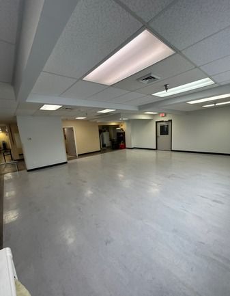 Empty, brightly-lit room with gray floor, white walls, and recessed lighting. Contains doorways, with light fixtures overhead.