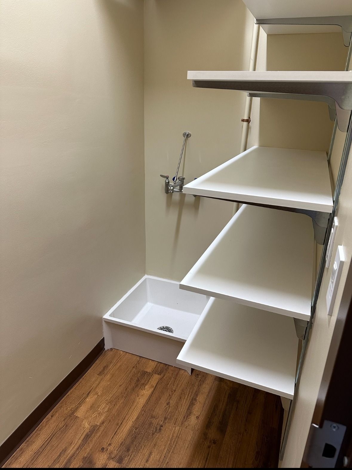 Laundry room with dog wash station: white shelves, tub, faucet against beige walls, brown floor.