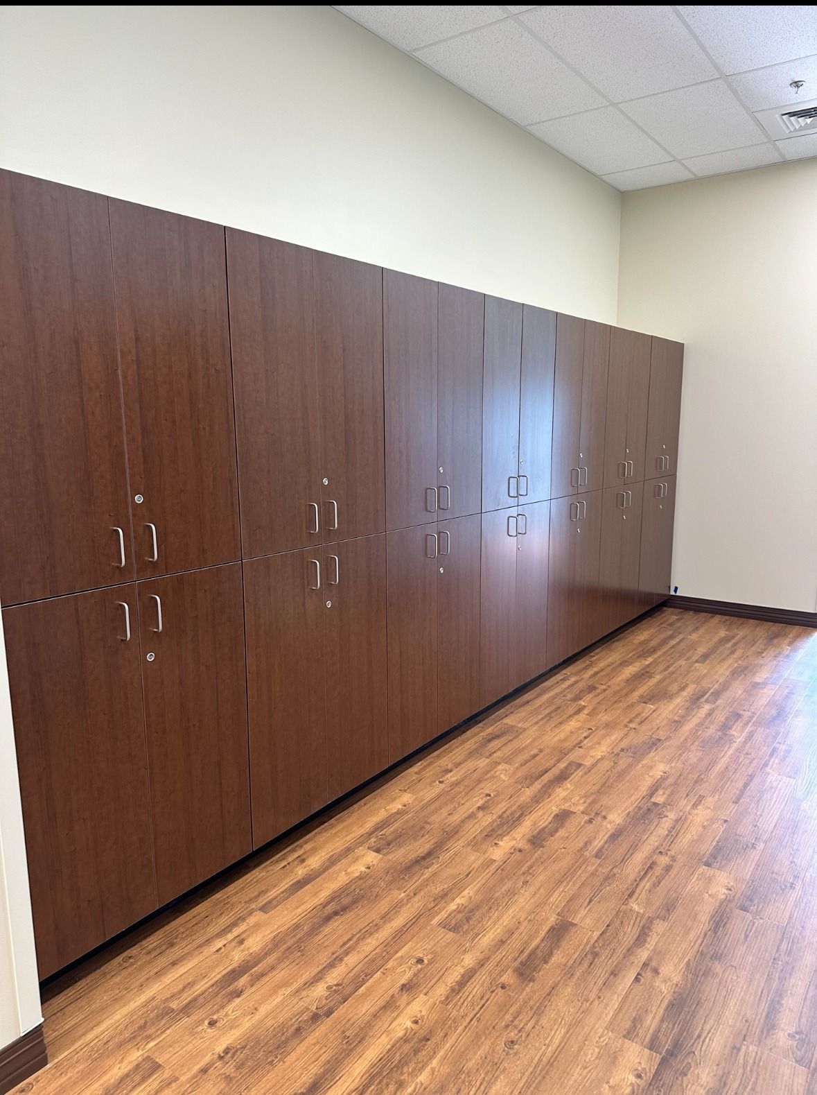 Row of tall, dark brown storage cabinets against a beige wall, over wood-look flooring.