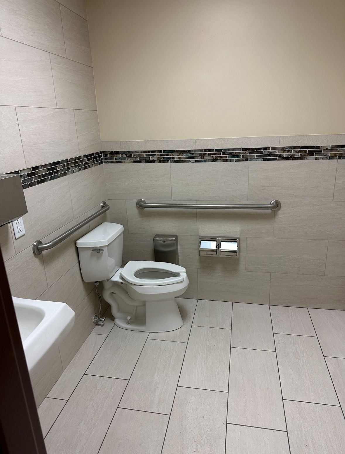 ADA-compliant public restroom with toilet, grab bars, and paper towel dispenser.