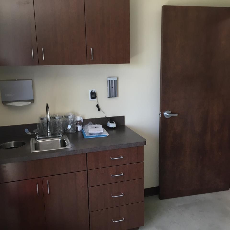 Examination room with brown cabinets, sink, and closed door.