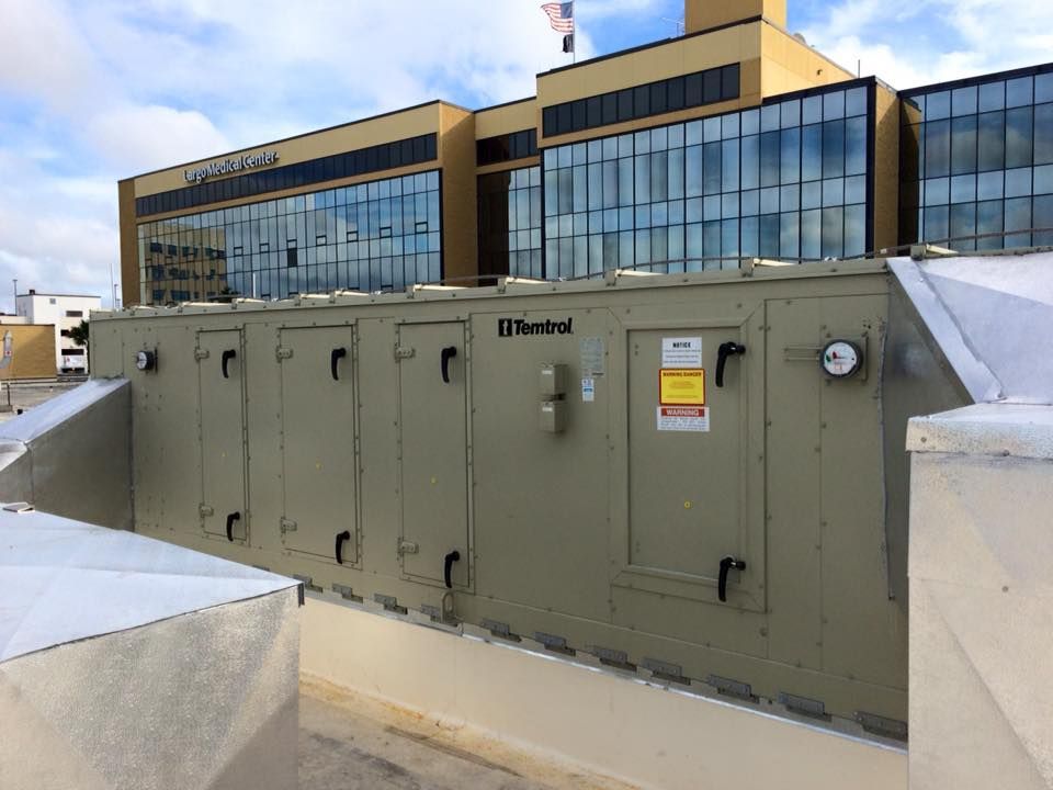 Rooftop HVAC unit on a building with a mirrored glass facade. Beige metal unit, partly snow-covered.