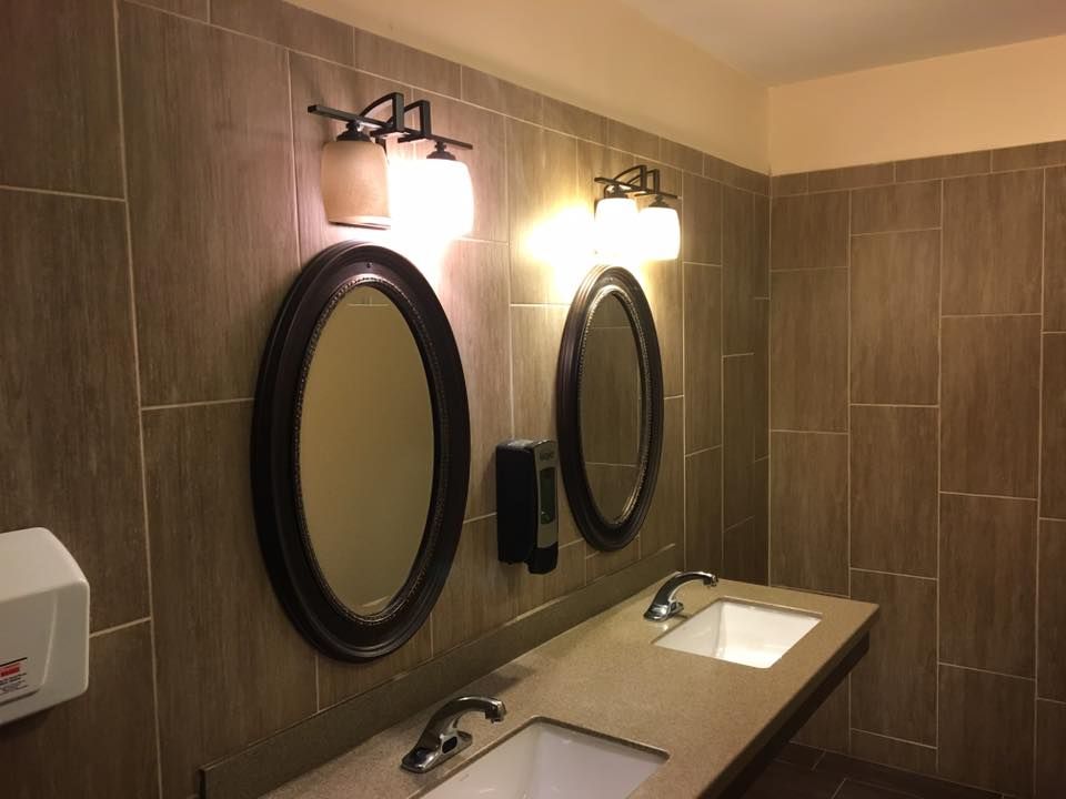 Public restroom with two sinks, oval mirrors, and sconce lighting.