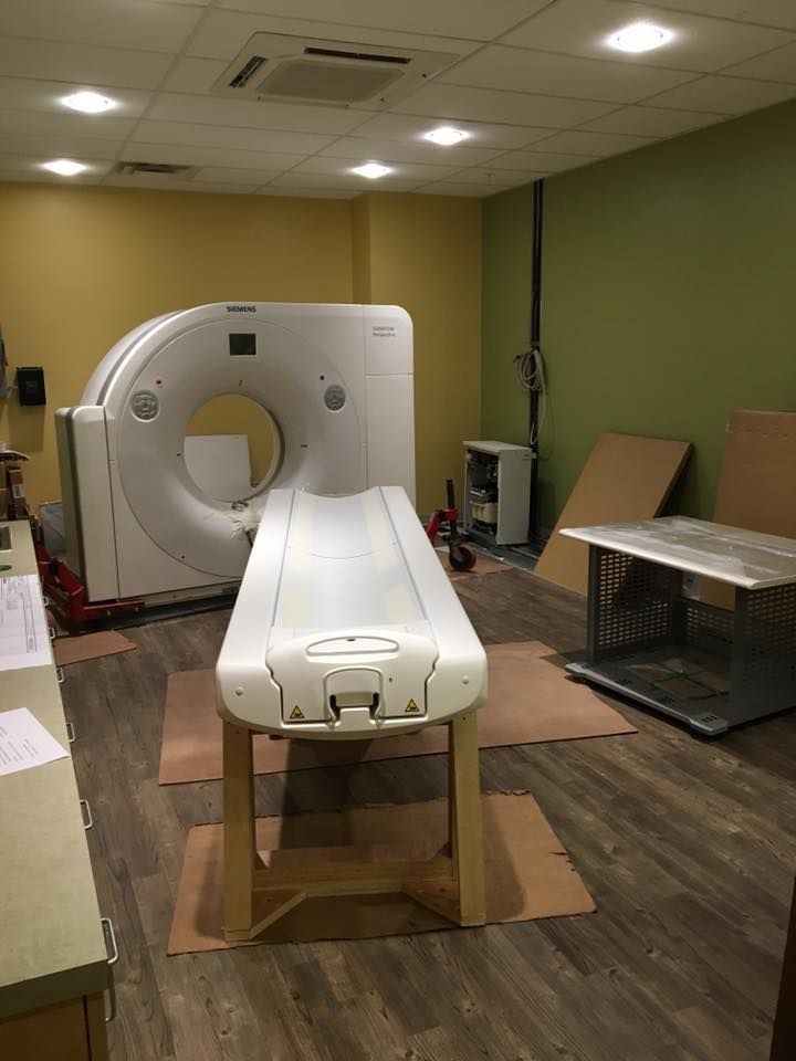 CT scanner in a medical room with an examination table, yellow and green walls, and brown flooring.