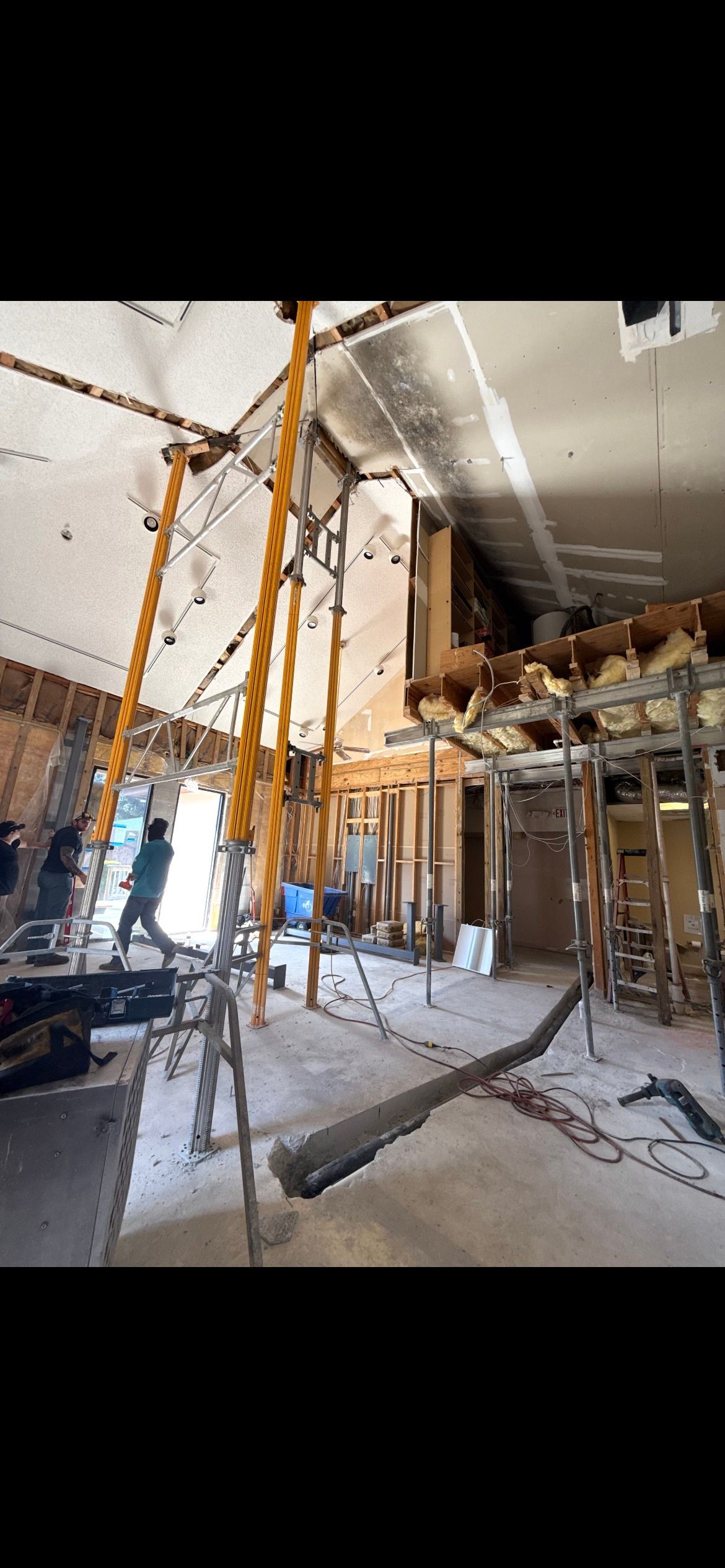 Interior of a building under construction, scaffolding supporting the ceiling. A worker is visible.