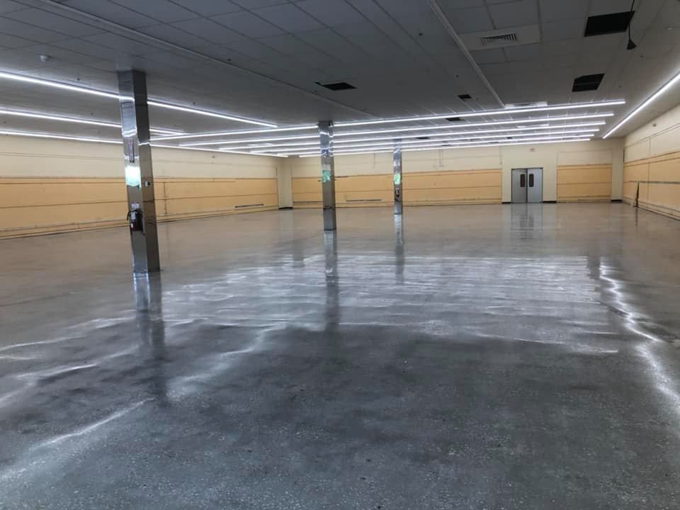 Large empty room with shiny concrete floor, pillars, and fluorescent lights.
