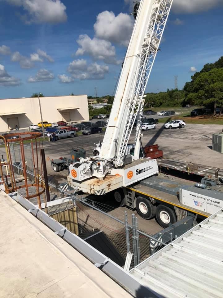 Crane lifting a piece of equipment from a roof opening, in an outdoor industrial setting.