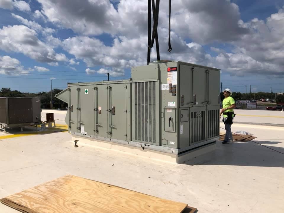 A rooftop HVAC unit being installed; a worker stands nearby under a cloudy sky.