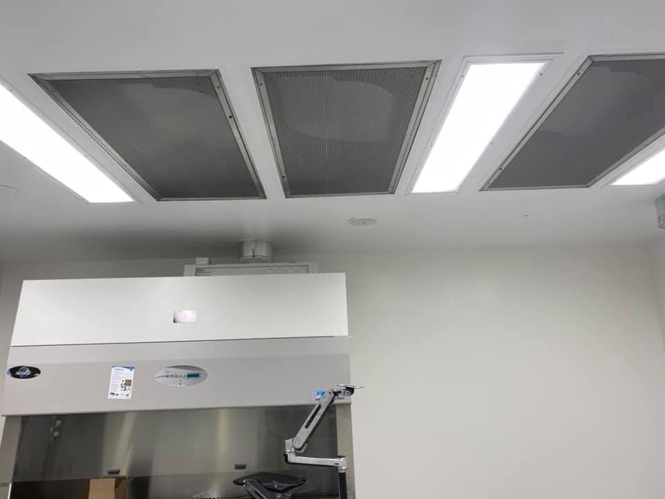 A clean room ceiling with air filtration, lab hood below. White walls, stainless steel.