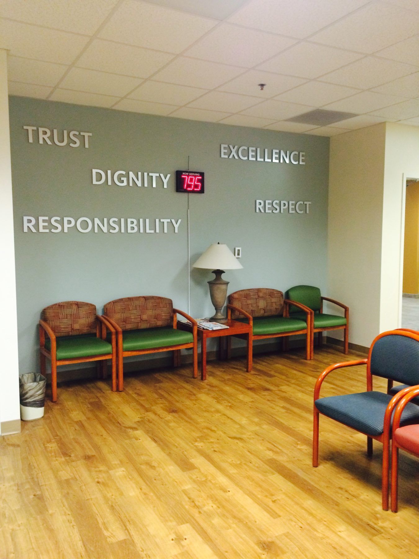 Waiting room with green and blue chairs, wooden floor, and a wall with values like "Trust" and "Dignity".