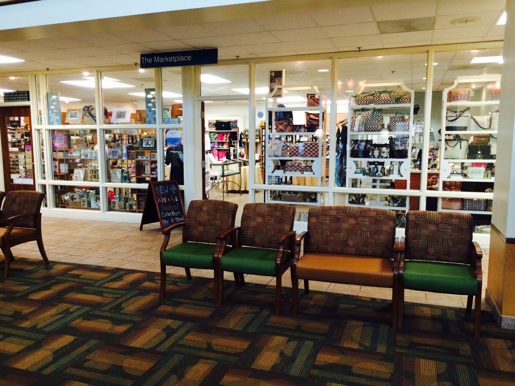 A row of green-cushioned chairs faces a storefront with shelves of items.
