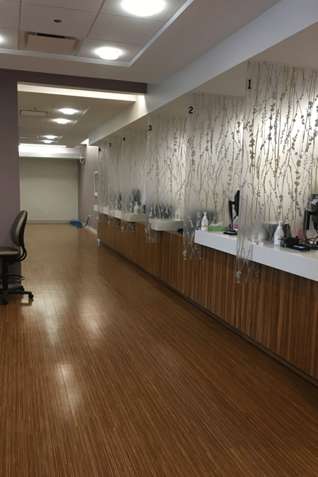 Long hallway with wood-look flooring and stations with clear dividers. Wall has abstract pattern; purple and white ceiling.