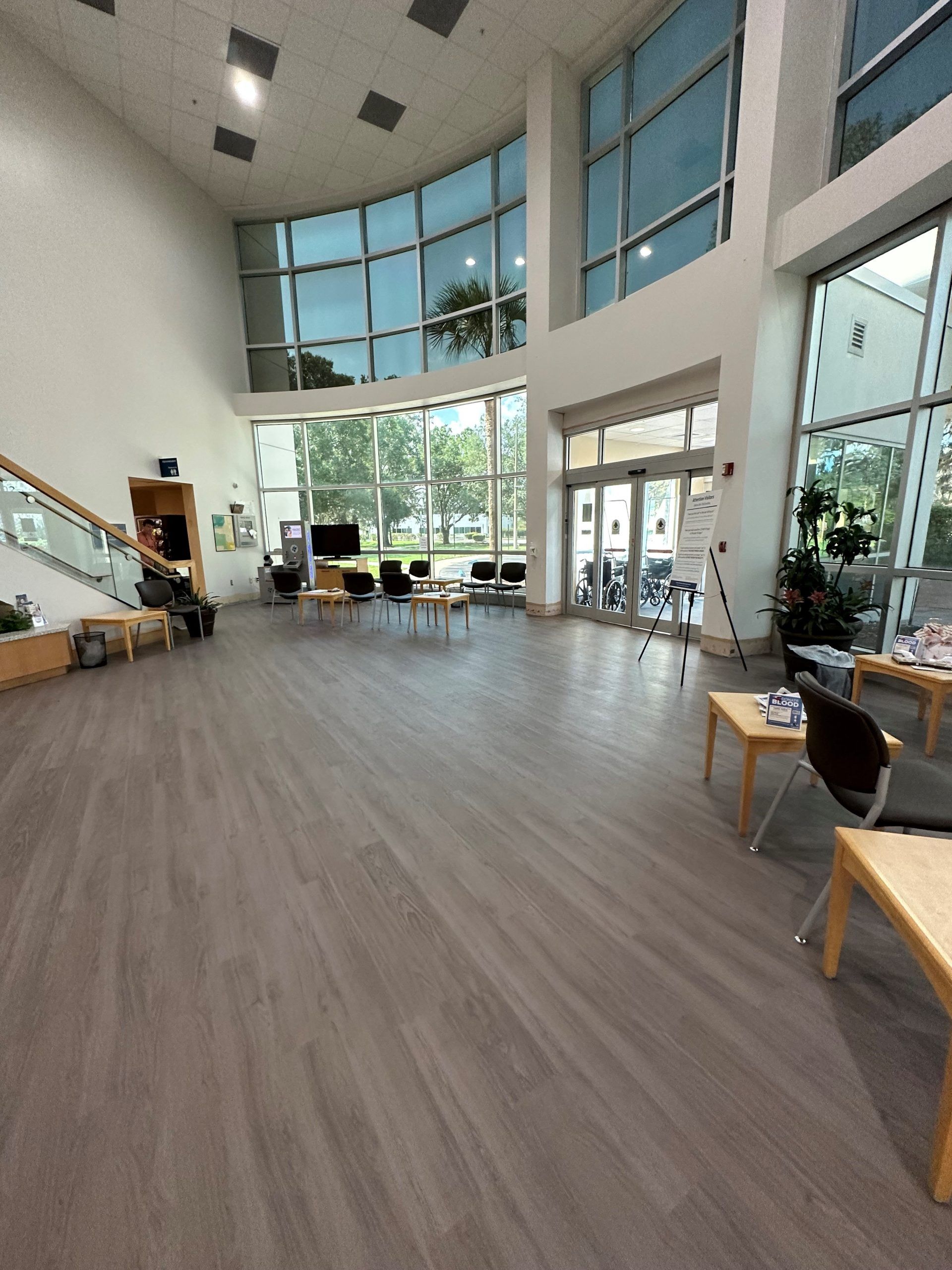 Spacious lobby with large windows, tables, and seating. Light-colored wooden floors.