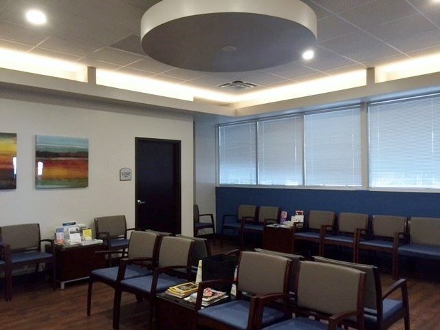 Waiting room with blue chairs, magazines, and artwork. Blue accent wall, windows with blinds.