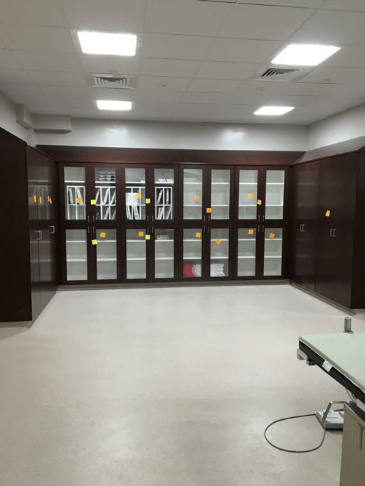 Dark wood storage cabinets with glass doors in a sterile, white-floored room, likely a medical setting.