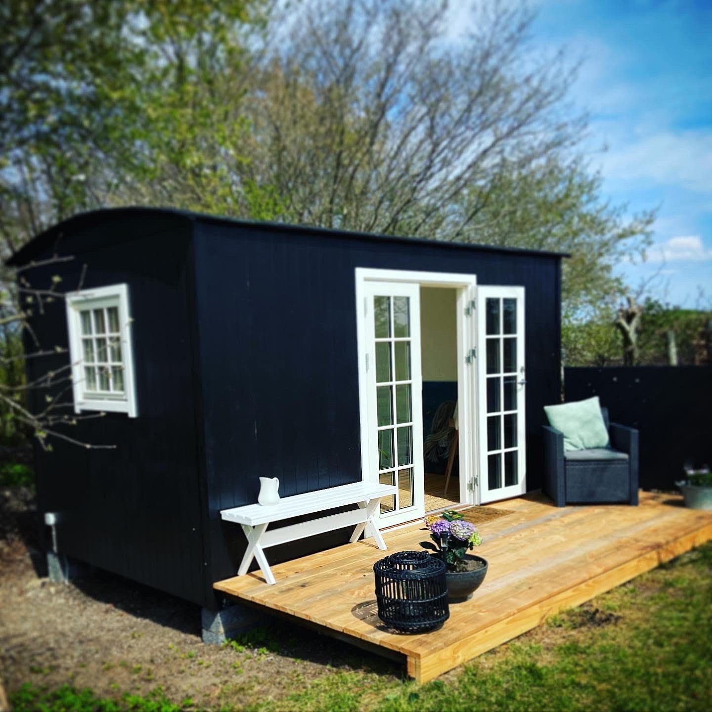 Et lille sort hus med et træterrasse foran.