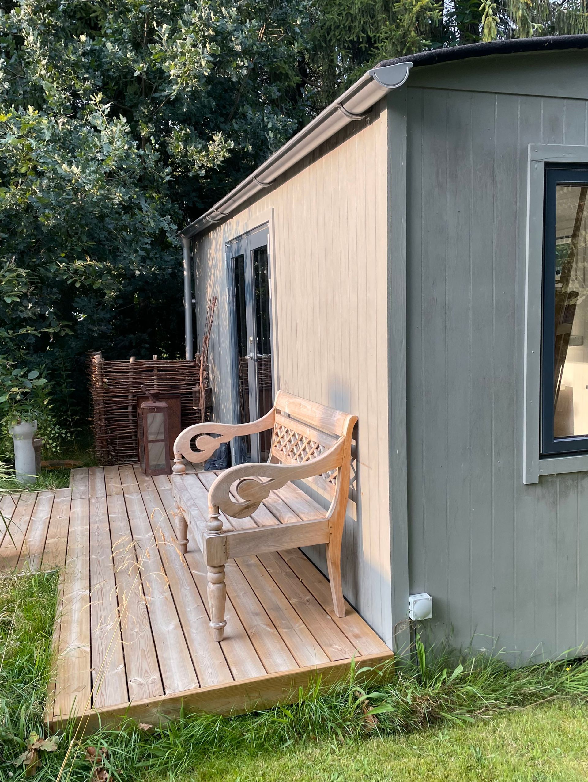 En træbænk står på et træterrasse ved siden af ​​et tiny house.