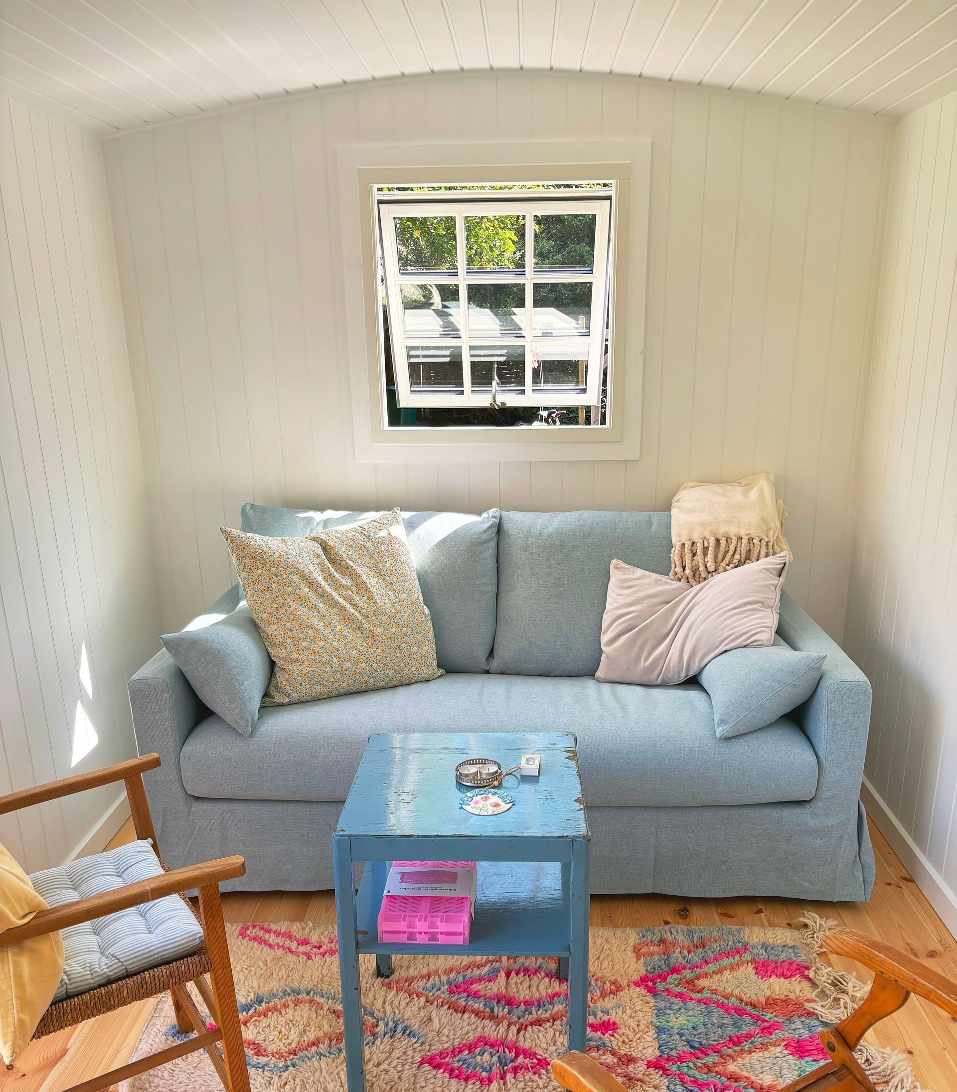 Inden i en skurvogn indrettet som stue med sofa, stol, bord. Et vindue står åbent.