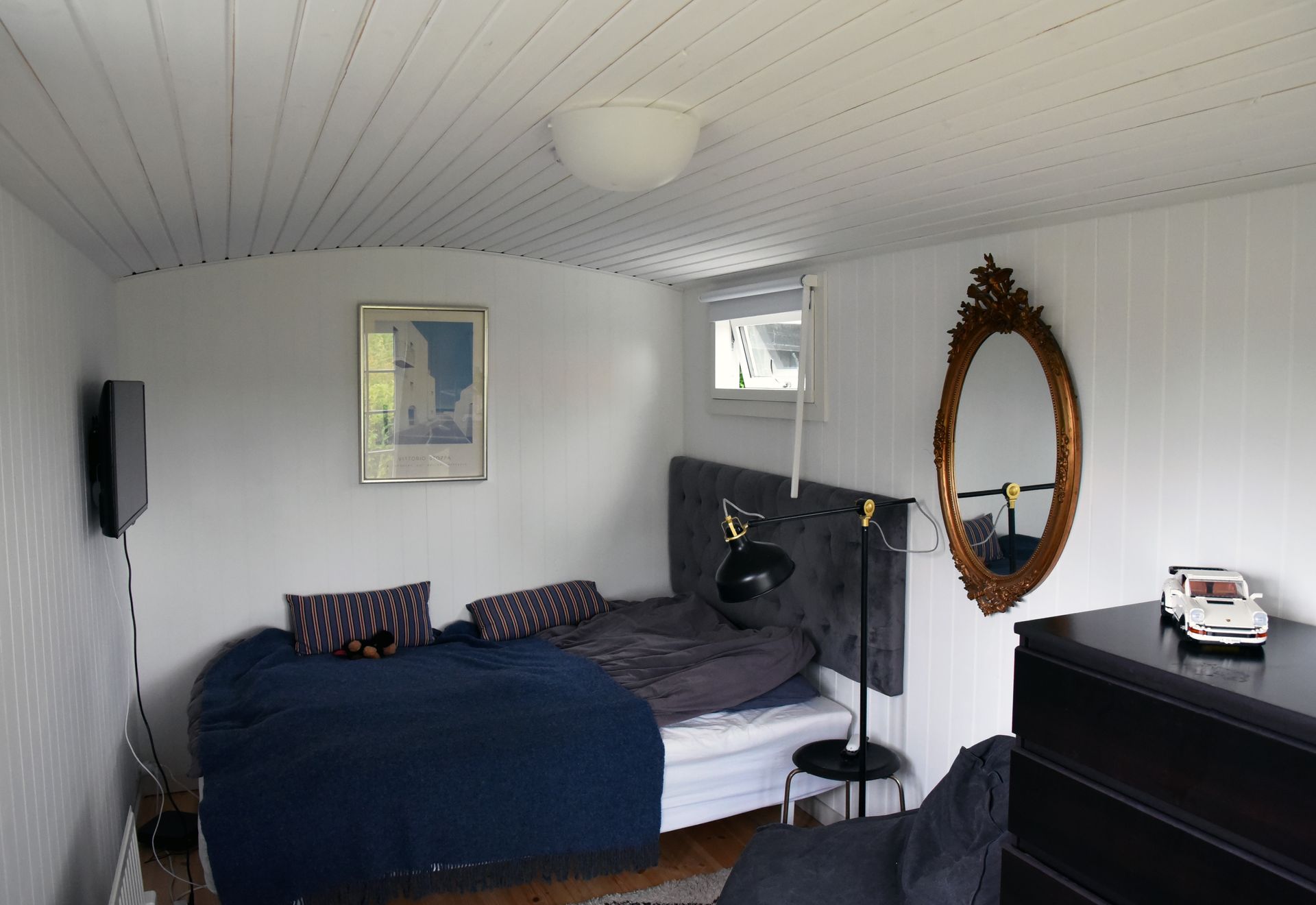 Indretning af et sommerhus anneks med en stor seng og et spejl på hvide vægge.