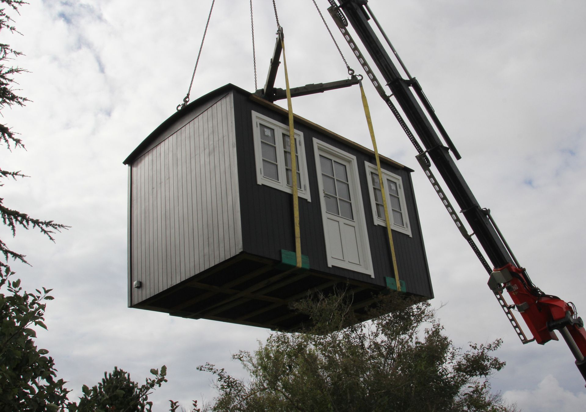 En kran løfter en skurvogn op i luften.