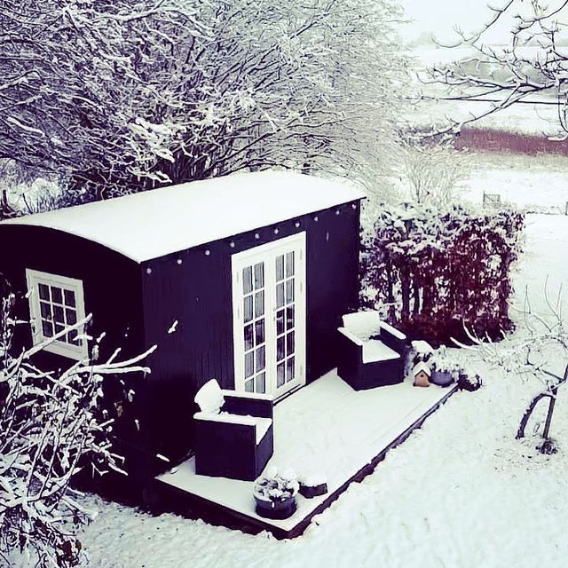 Et sort tiny house med en veranda og stole i sneen.