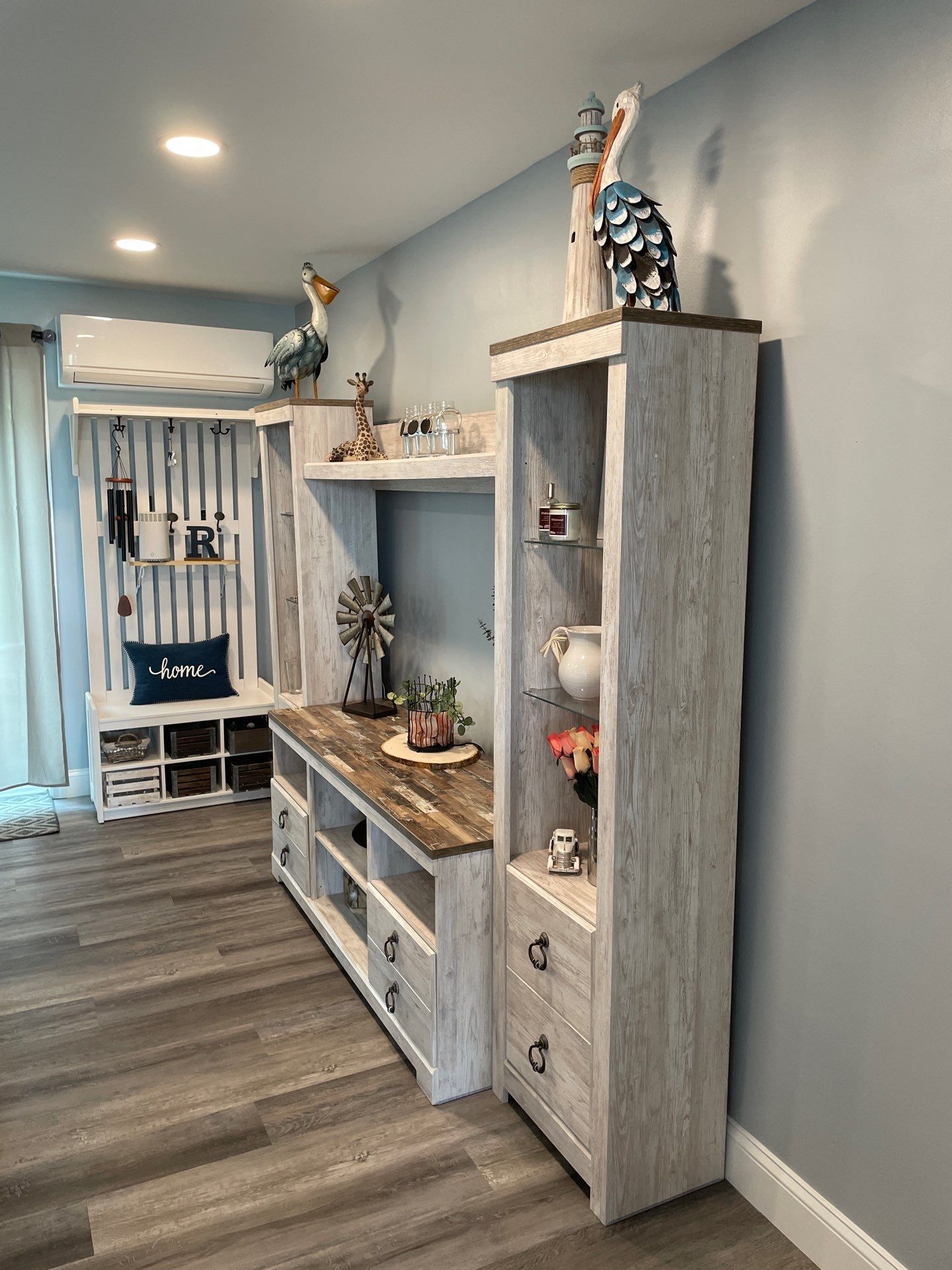 Living room with white distressed wood entertainment center and built-in bench. Decor includes bird sculptures and a windmill.
