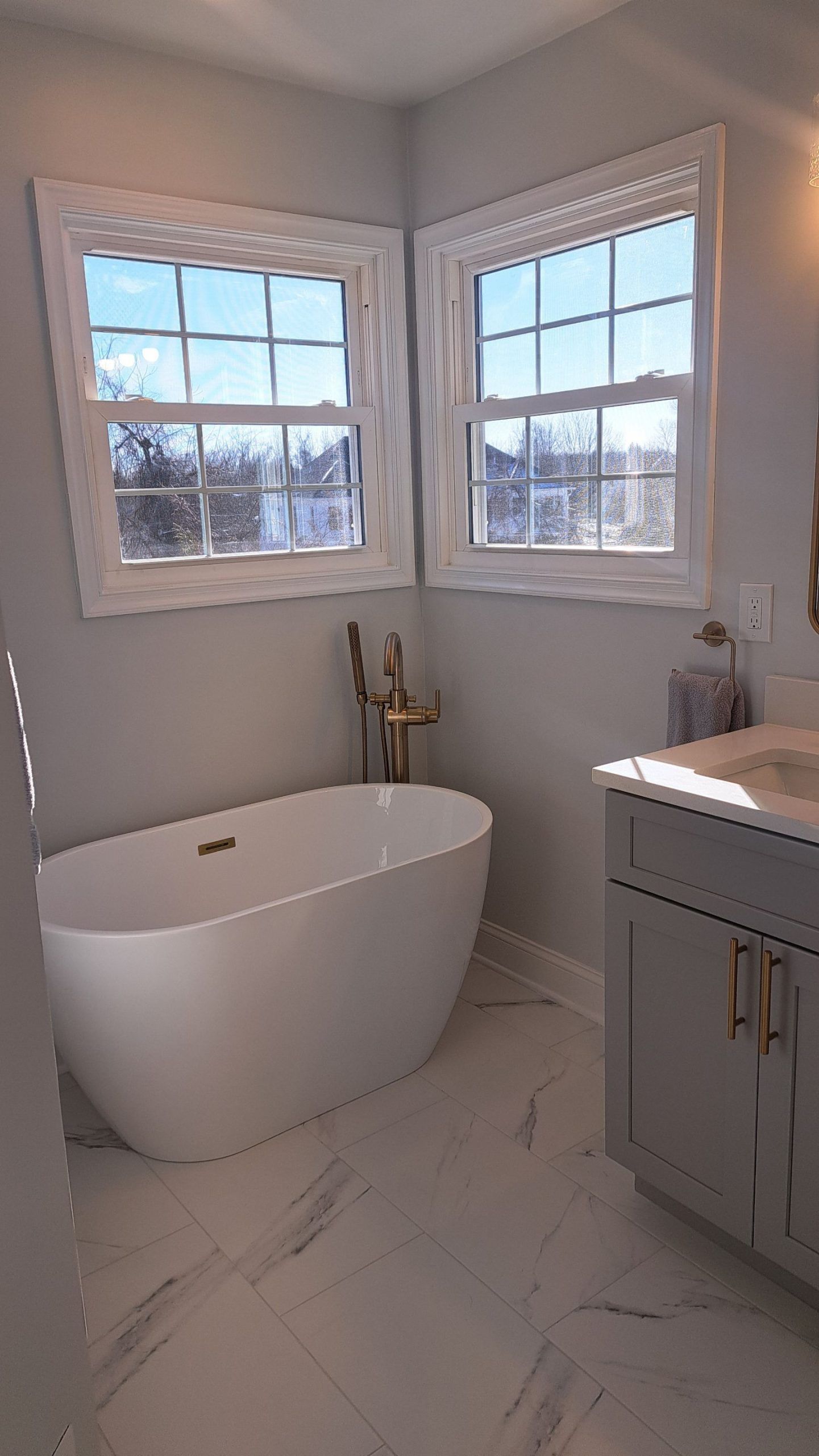 Bathroom with white oval tub, windows, and gray vanity. Sunlight streams in.
