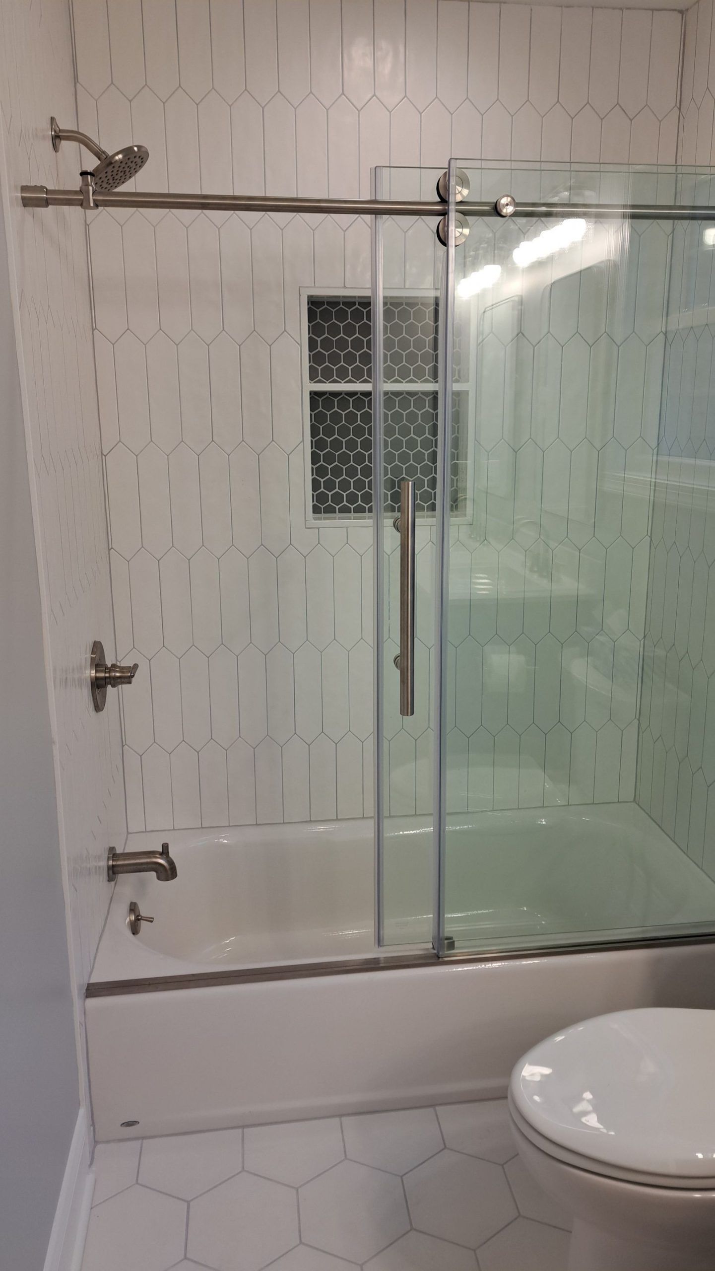Bathroom with white hexagon tiles and a glass sliding shower door.