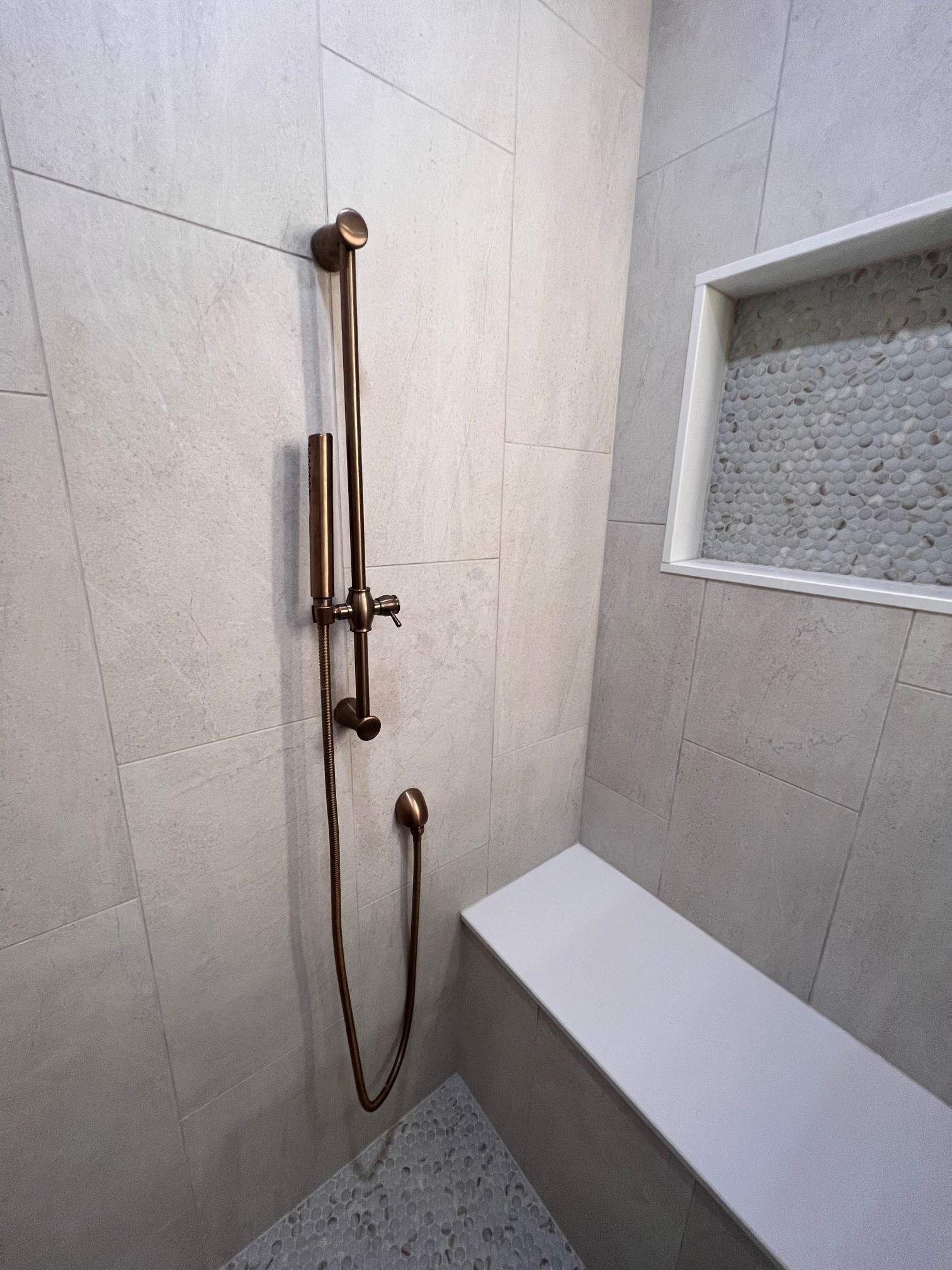 A modern shower with bronze fixtures, light gray tiles, a built-in bench, and a tiled niche.