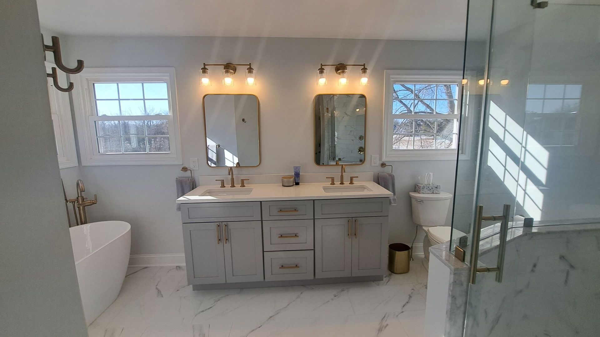 Bathroom with gray vanity, two mirrors, and a glass shower door.