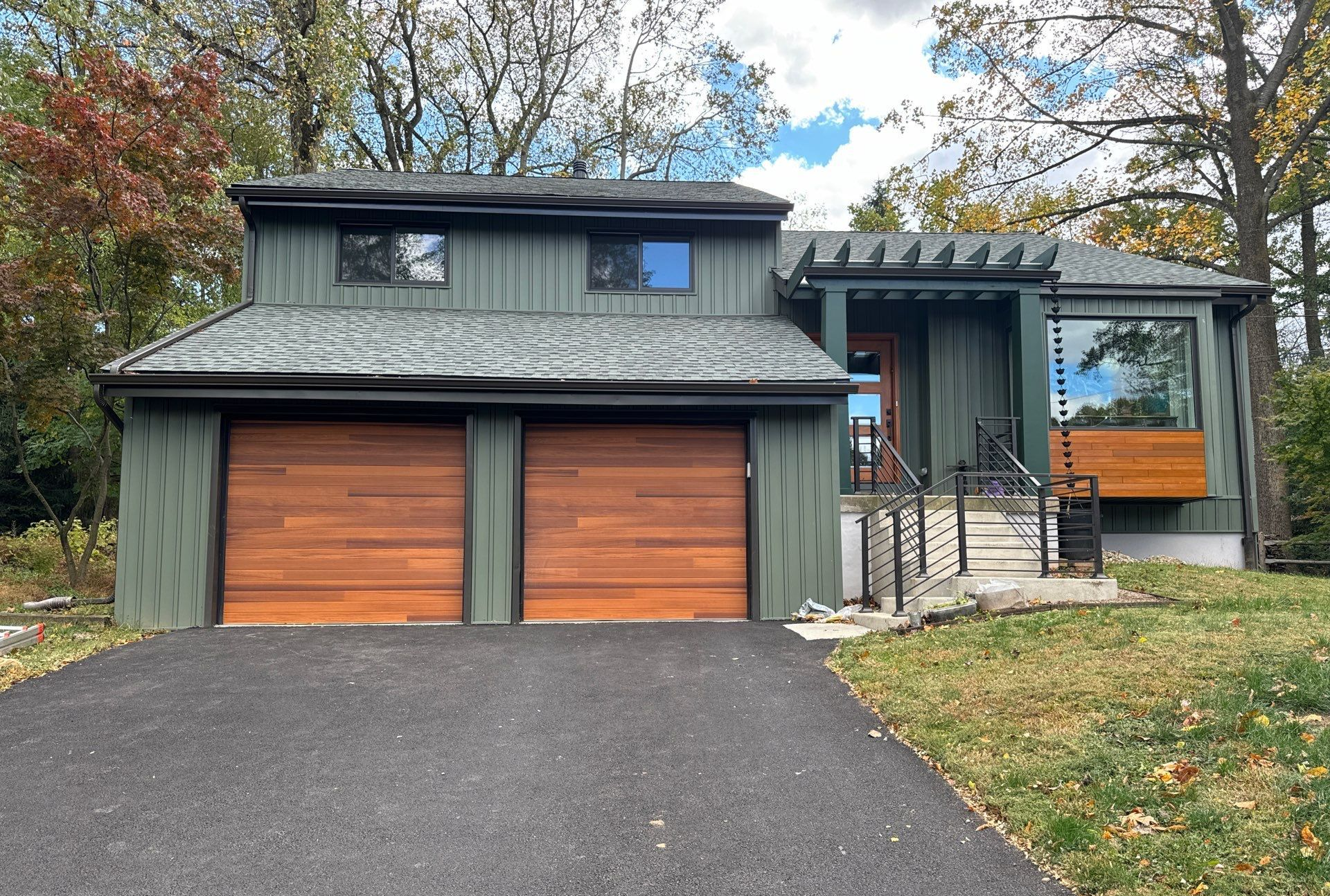 Green house with wood garage doors, driveway, and front door with porch.
