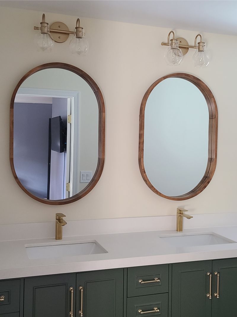 Bathroom with two oval mirrors, gold fixtures, and green cabinets.